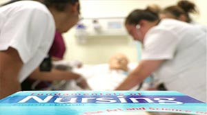 Nursing students in a skills lab with a textbook in the foreground